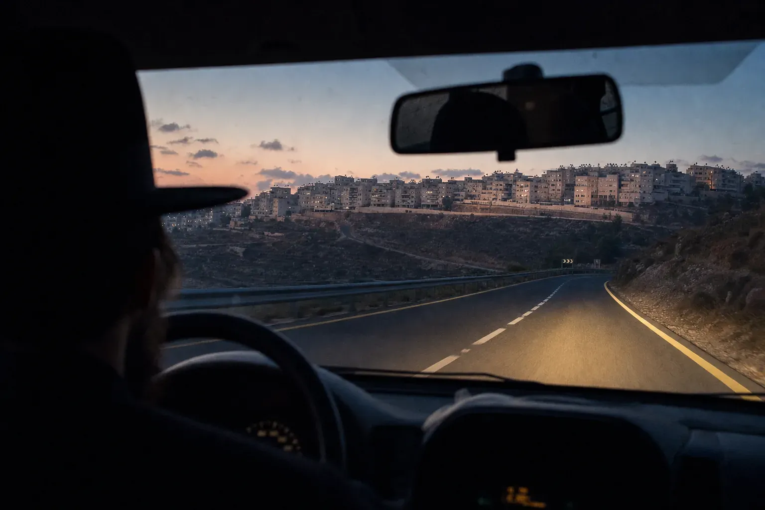 The road to a hill town at dawn, seen through the front window of a car