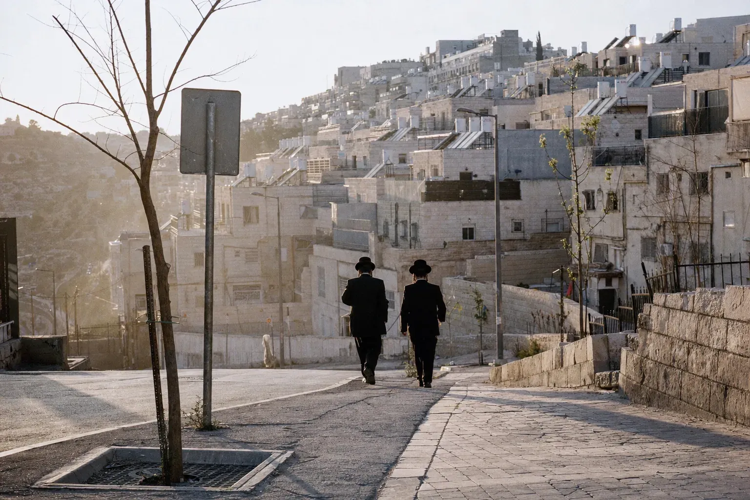 A hillside street in Beitar Illit at late afternoon, Jerusalem-stone apartment blocks, two men walking downhill