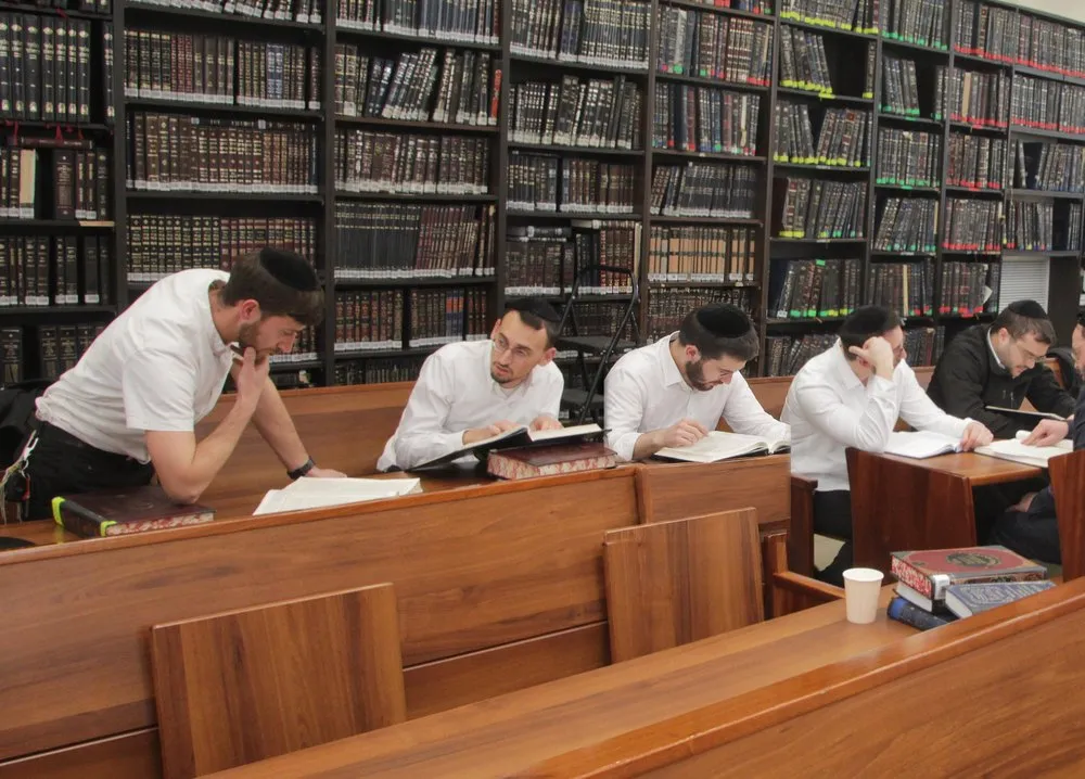 Yungeleit learning at long wooden tables under walls of sefarim at Toras Avrohom Zev, Beitar Illit