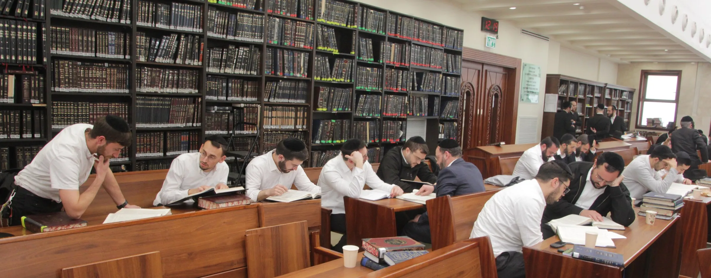 Yungeleit learning at long wooden tables under walls of sefarim at Toras Avrohom Zev, Beitar Illit