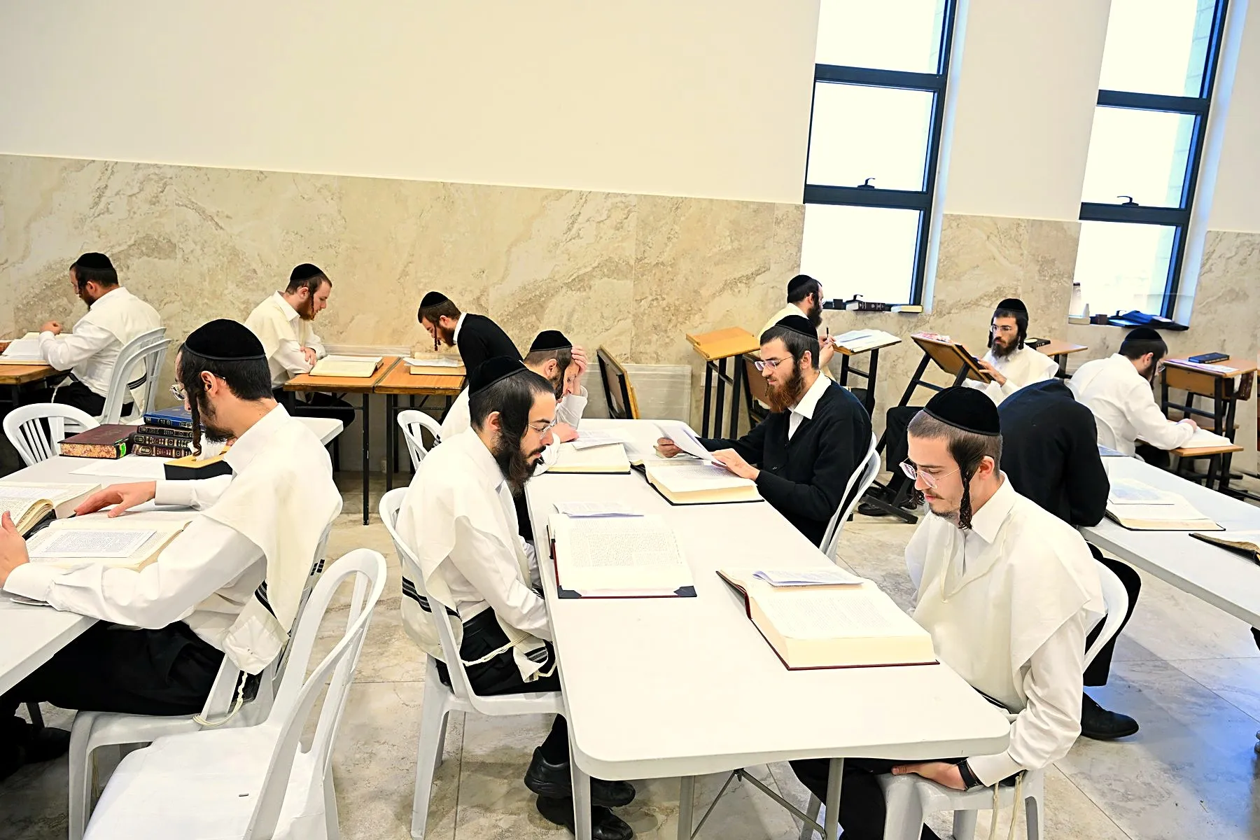 Yungeleit learning in chavrusos at white tables in a bright hall at Zichron Leib, Beitar Illit