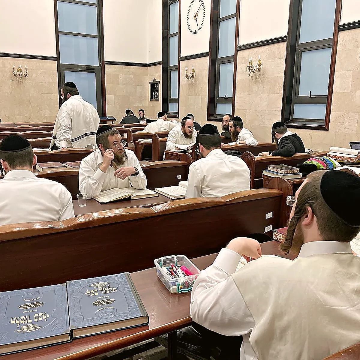 A full beis medrash, sefarim open along every bench, daylight from tall windows