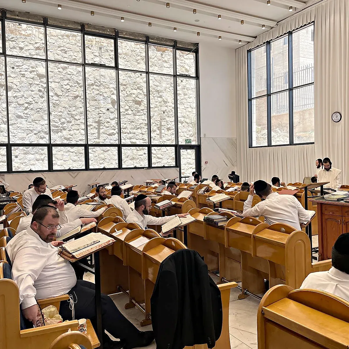 A packed beis medrash, every shtender taken, tall stone-framed windows along the wall